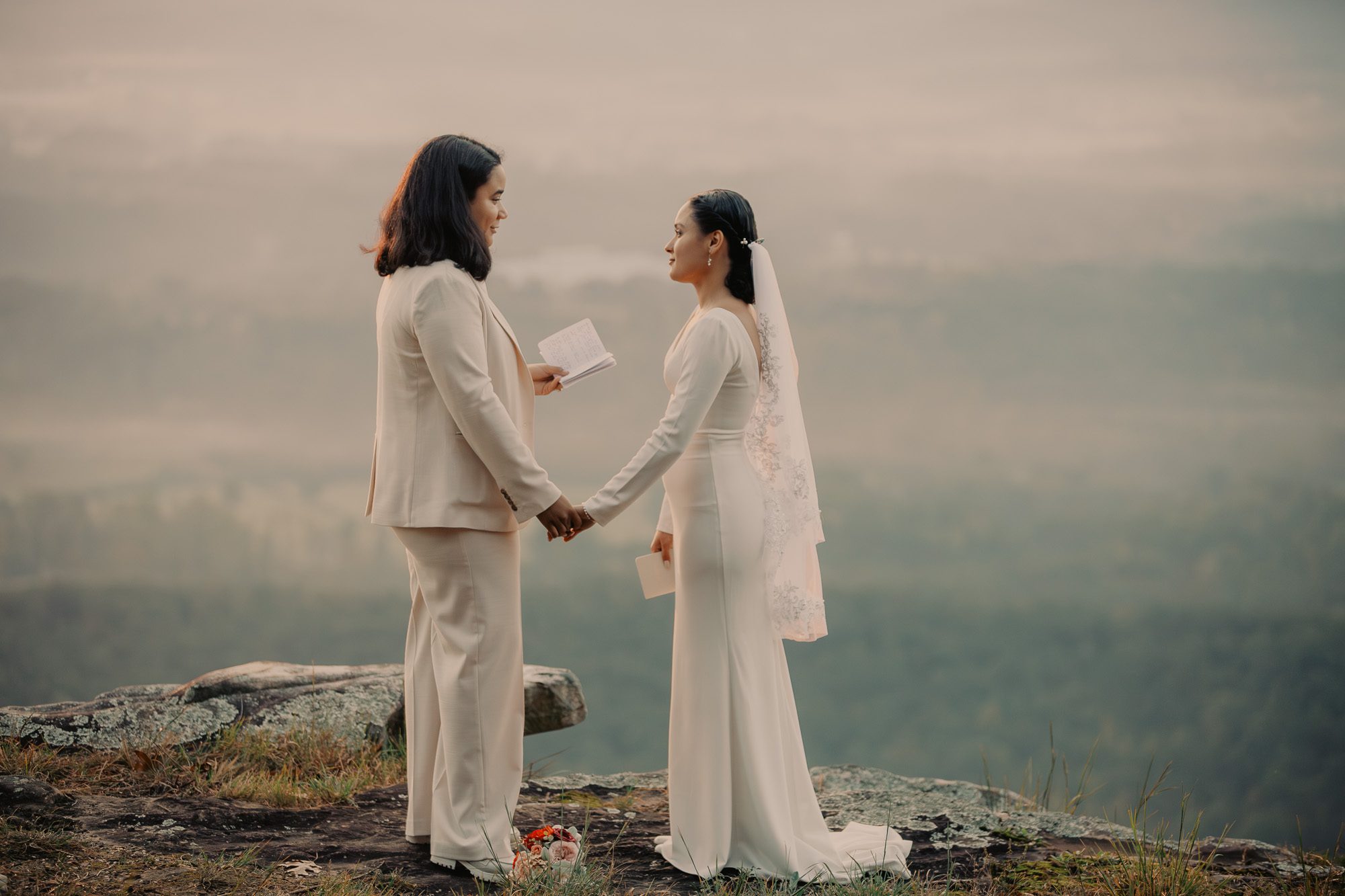 At sunrise in Cloudland Canyon, a same-sex couple in a white suit, and a white dress stand hand-in-hand, tears flowing during their heartfelt  elopement.