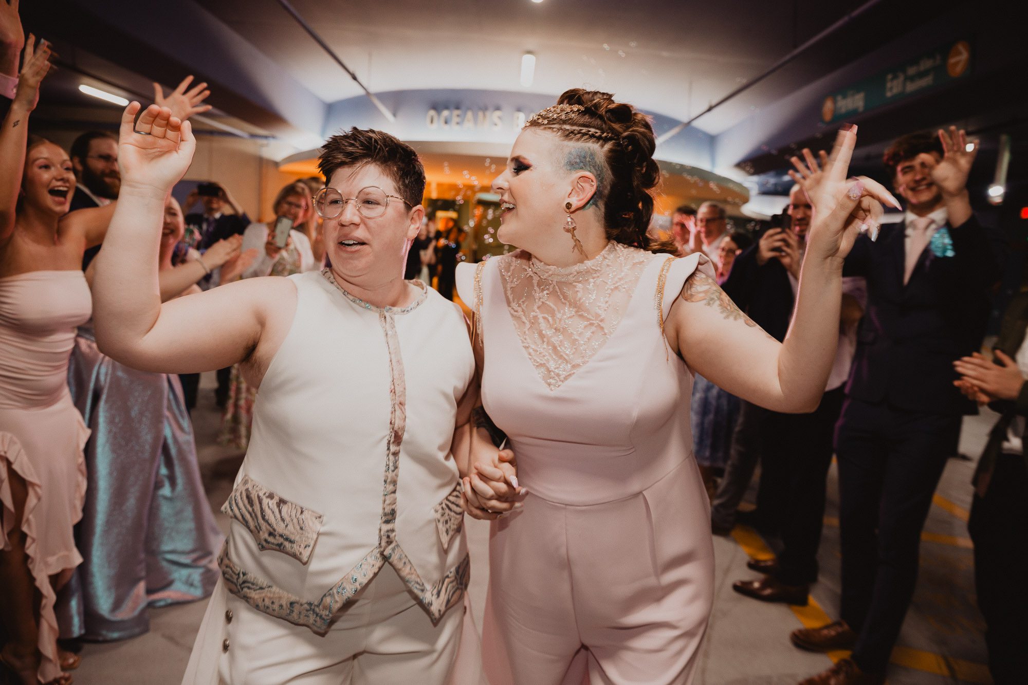 a newlywed LGBTQ couple makes their wedding day grand exit from the Georgia Aquarium, waving to their guests and laughing while arm in arm