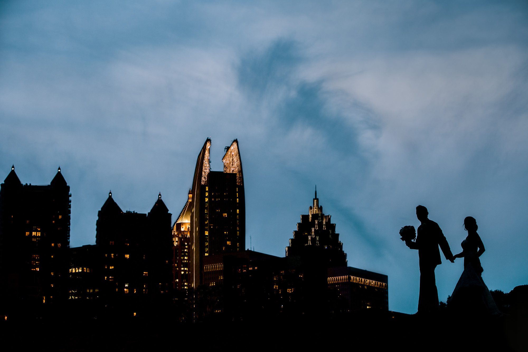 a newlywed couple is silhouetted against the evening sky in front of the midtown Atlanta skyline