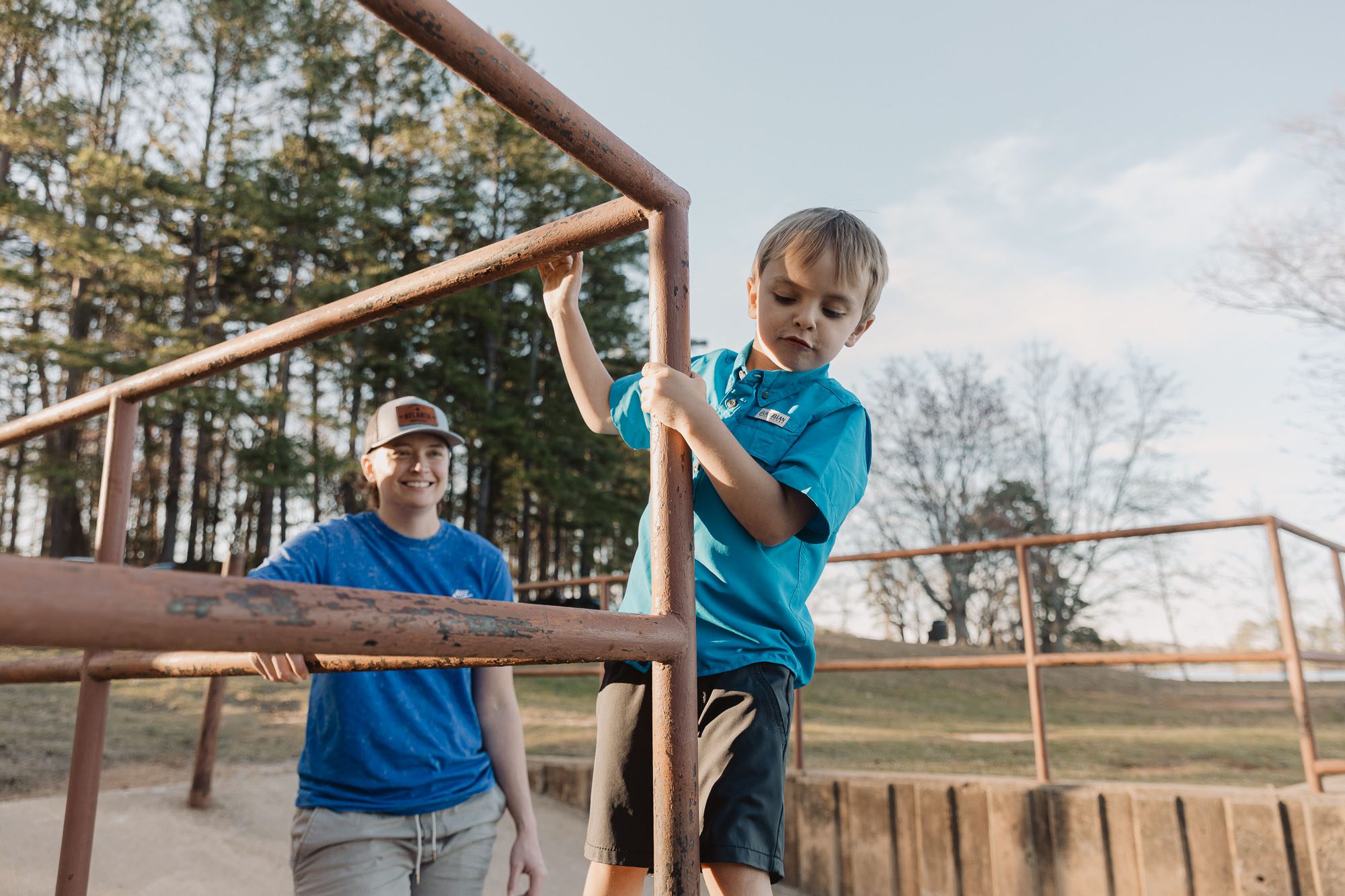 a mother watches her small child climb on a railing on the beach at Lake Lanier during their lifestyle family photo session