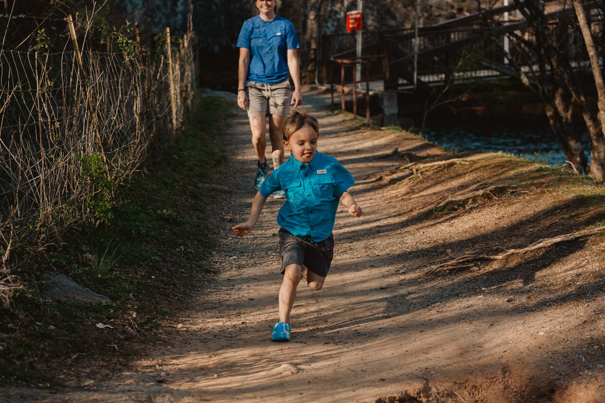 a small child runs at full speed while his mother walks calmly behind him on a path at a local metro atlanta park during their active lifestyle family photo session