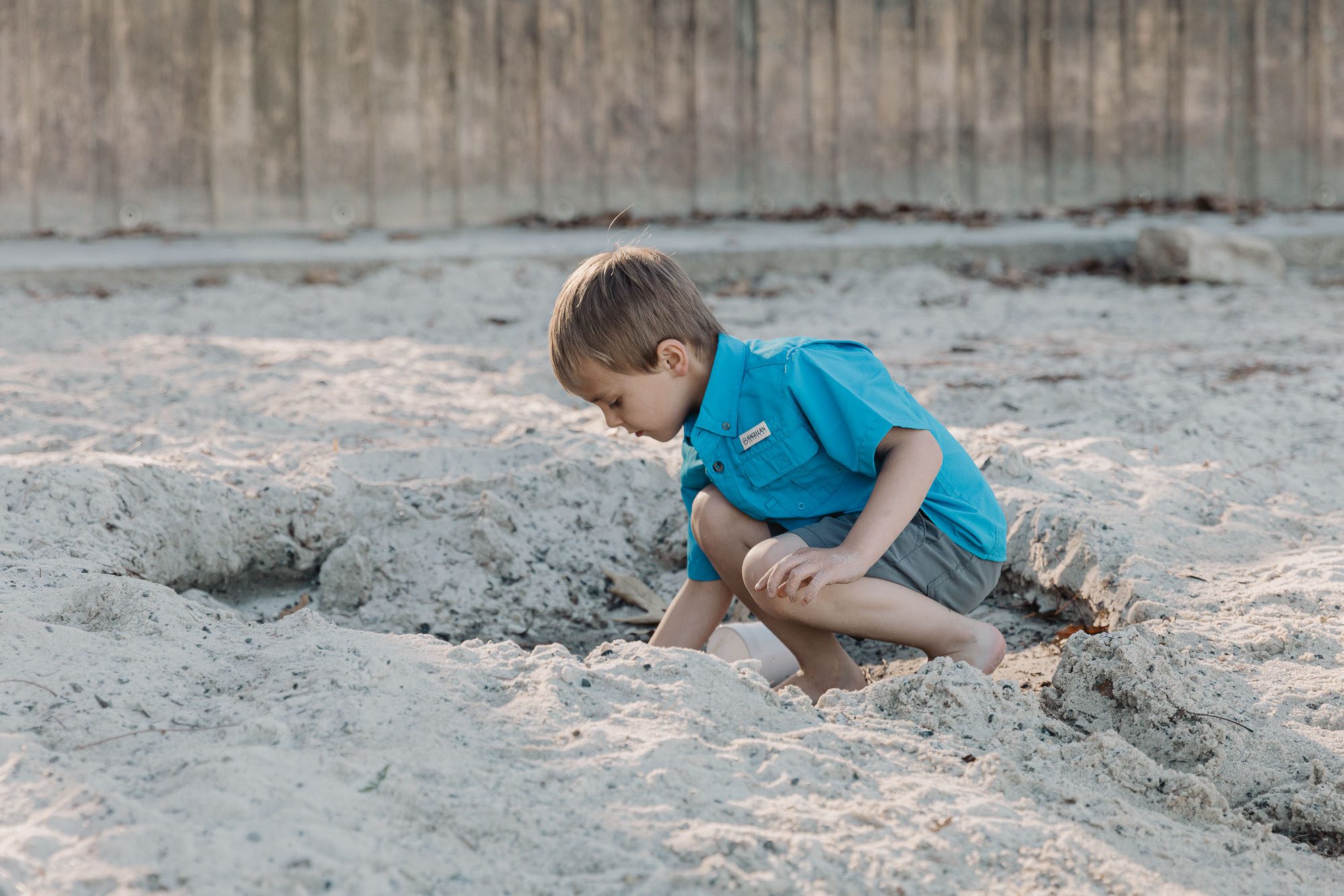 a small child digs a hold in the sand on the beach at Lake Lanier during a lifestyle family photo session