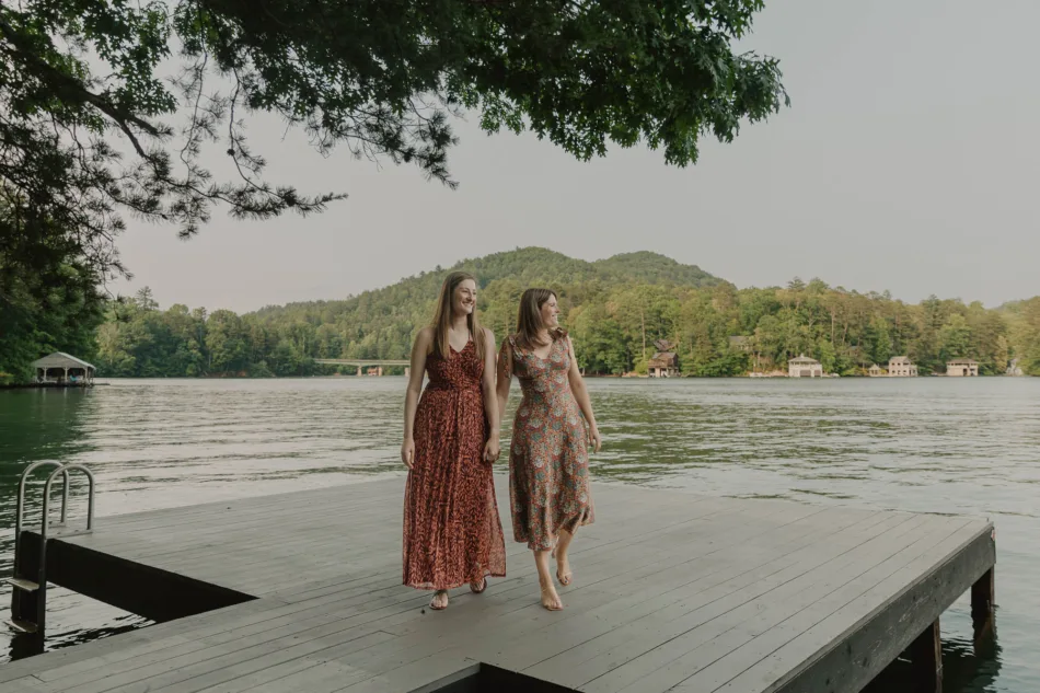 Two women walk hand-in-hand across a dock on the lake after a romantic Lakeside lgbtq proposal in north Georgia