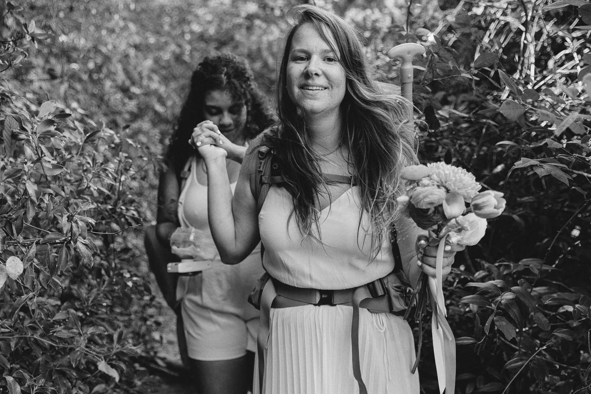 two brides wearing white and holding hands hike to the bamboo forest on the chattahoochee river in atlanta to have their wedding