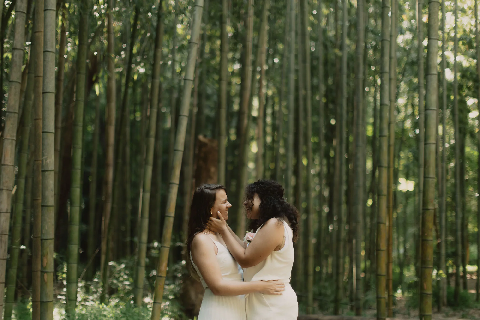 two brides wearing white embrace on their wedding day in the bamboo forest on the chatahoochee river in atlanta