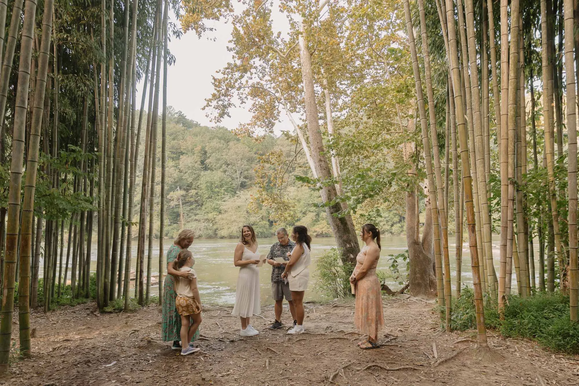 two brides wearing white are surrounded by close family at their ceremony on their wedding day in the bamboo forest on the chattahoochee river in atlanta