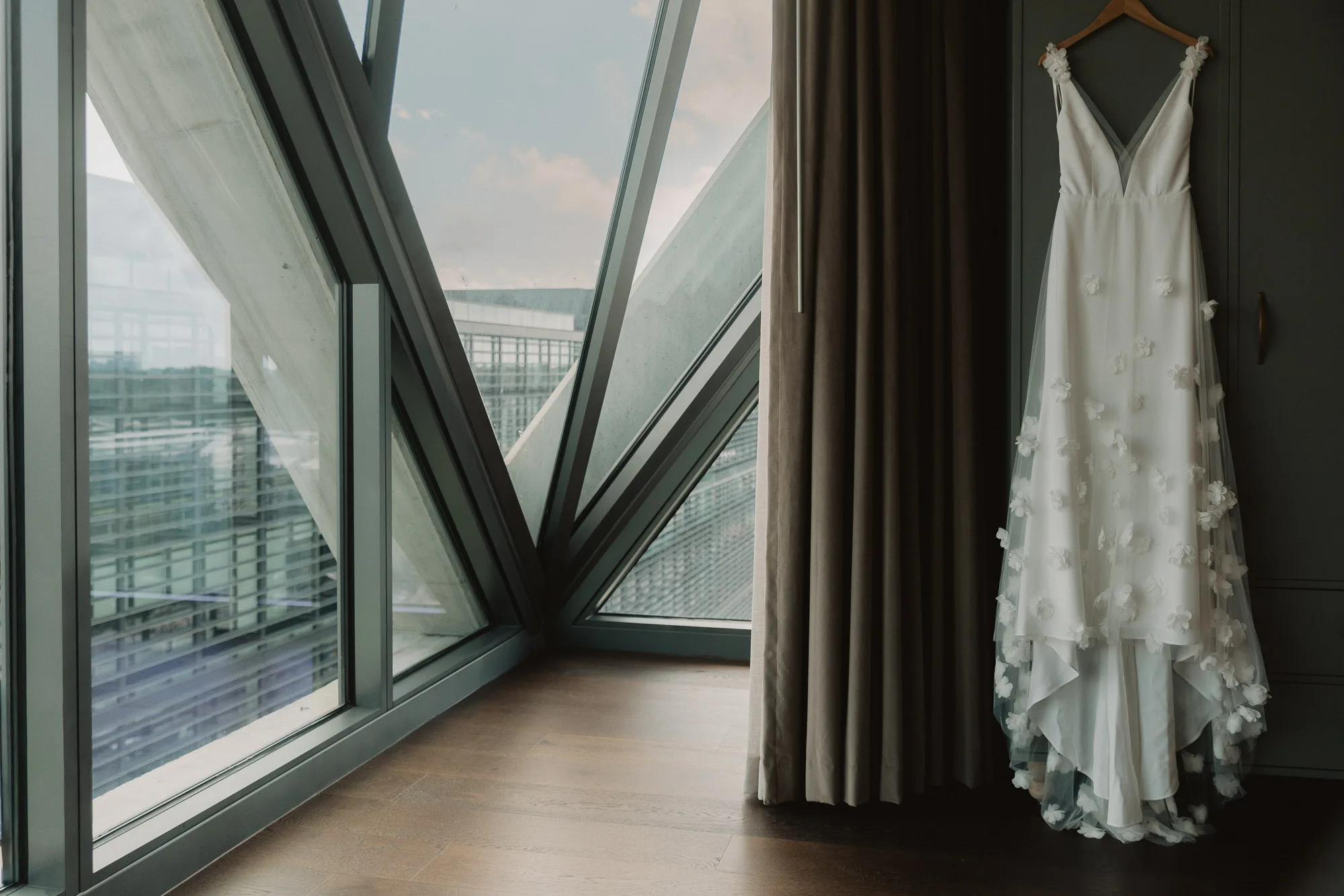 a white wedding dress hangs on a closet next to a window overlooking Atlanta in the Forth Hotel