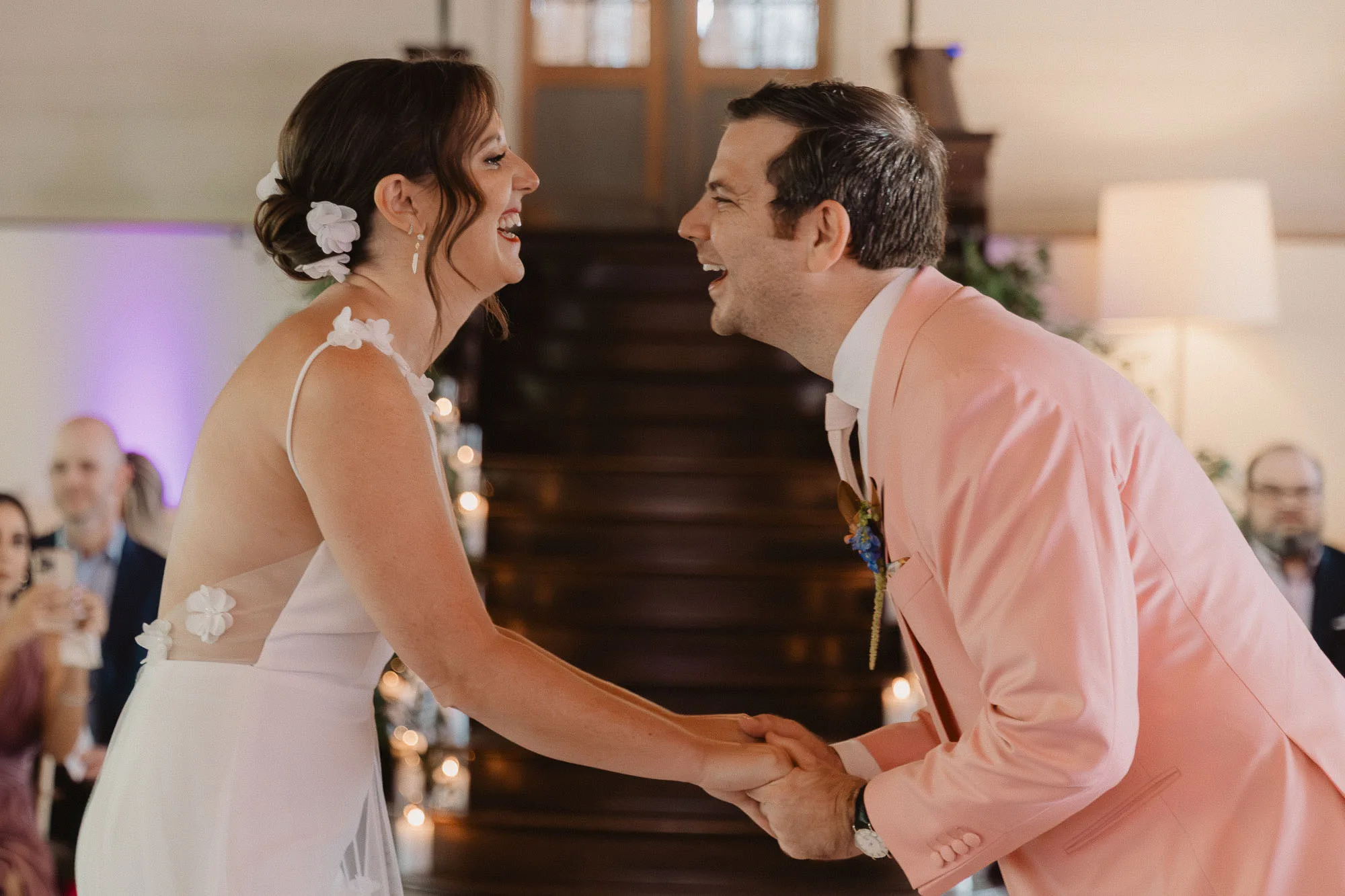 a bride wearing a white dress and a groom wearing a pink tuxedo hold hands and laugh happily during their wedding ceremony at Summerour Studio in Atlanta