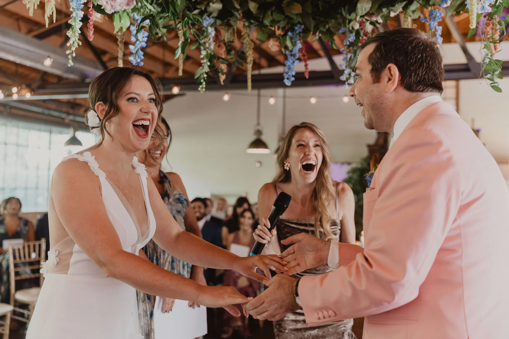 a bride wearing a white dress and a groom wearing a pink tuxedo hold hands and laugh happily during their wedding ceremony at Summerour Studio in Atlanta