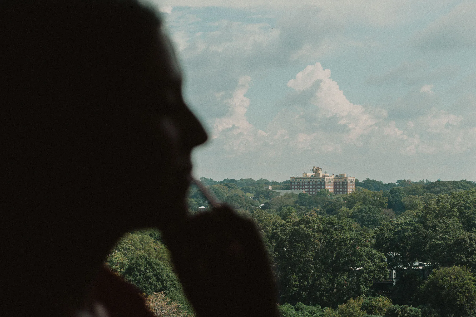 the face of a bride having her wedding day makeup applied is silhouetted in front of a high floor hotel window view of atlanta