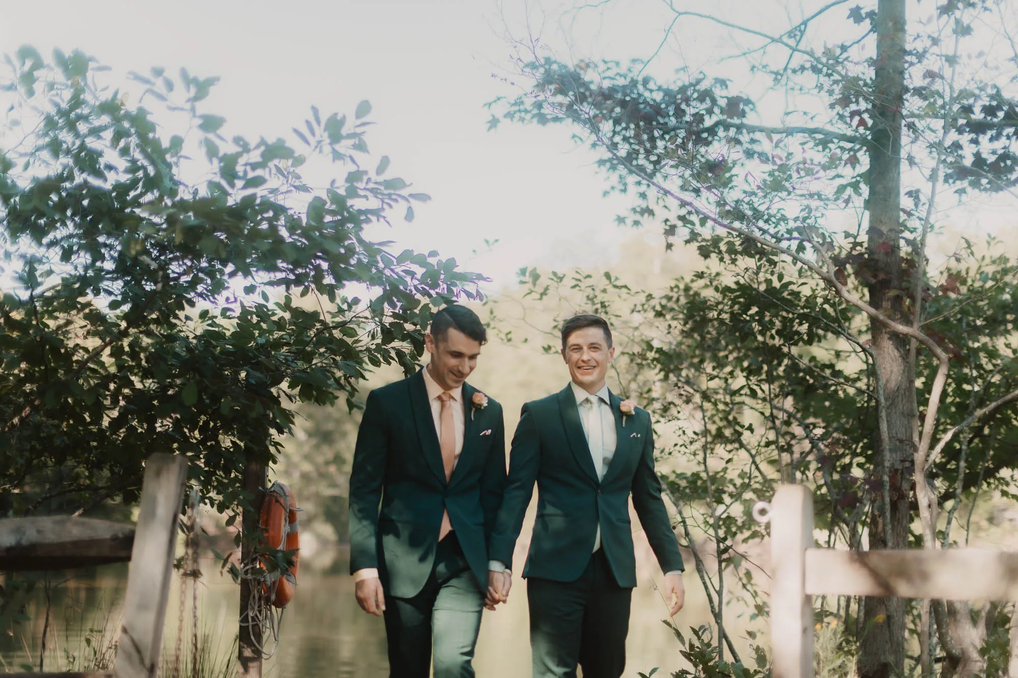 two grooms wearing green suits hold hands and walk together at their atlanta wedding