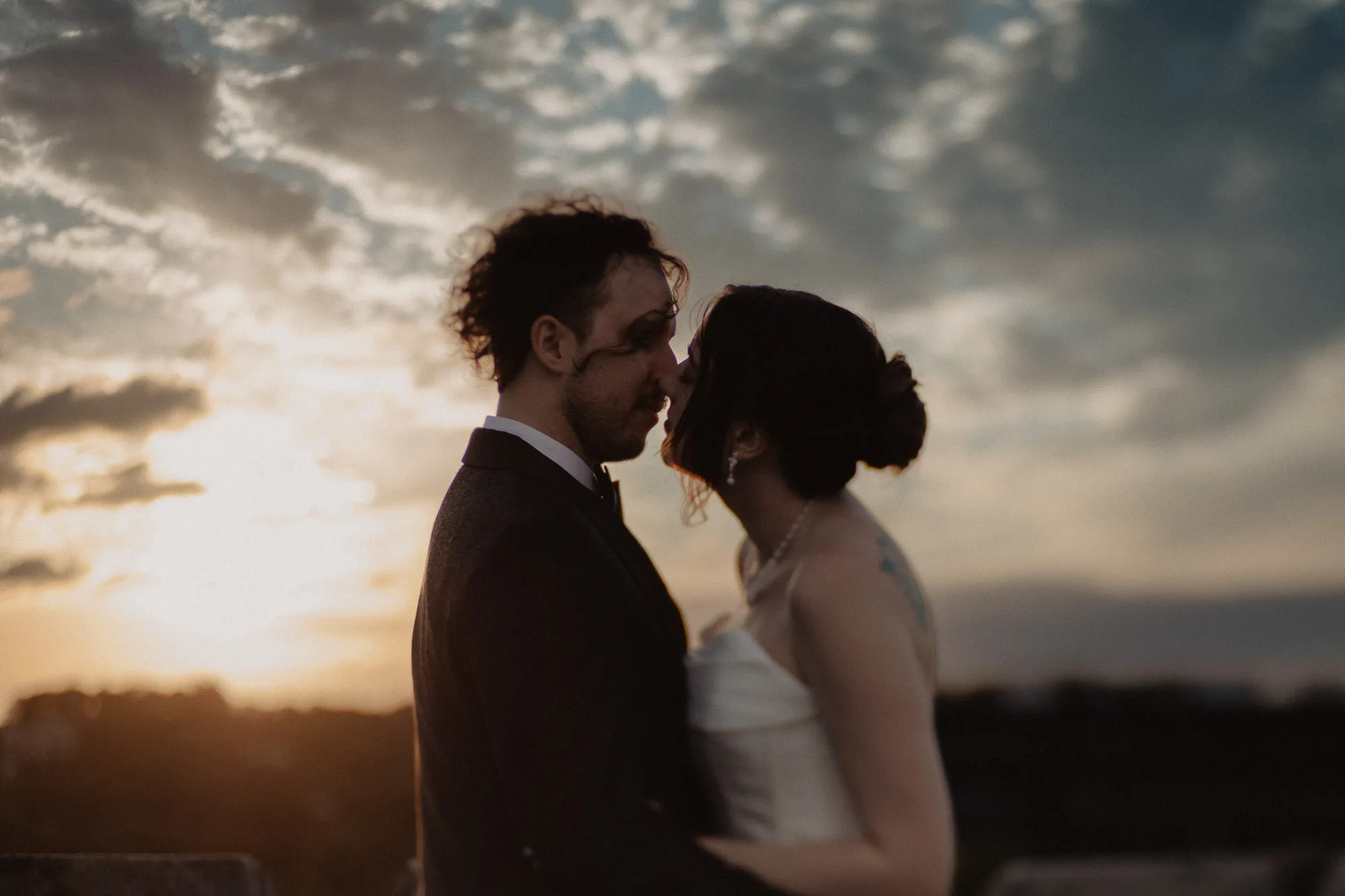 a bride and groom lean in for a kiss in front of a dramatic sunset sky on their wedding day in atlanta